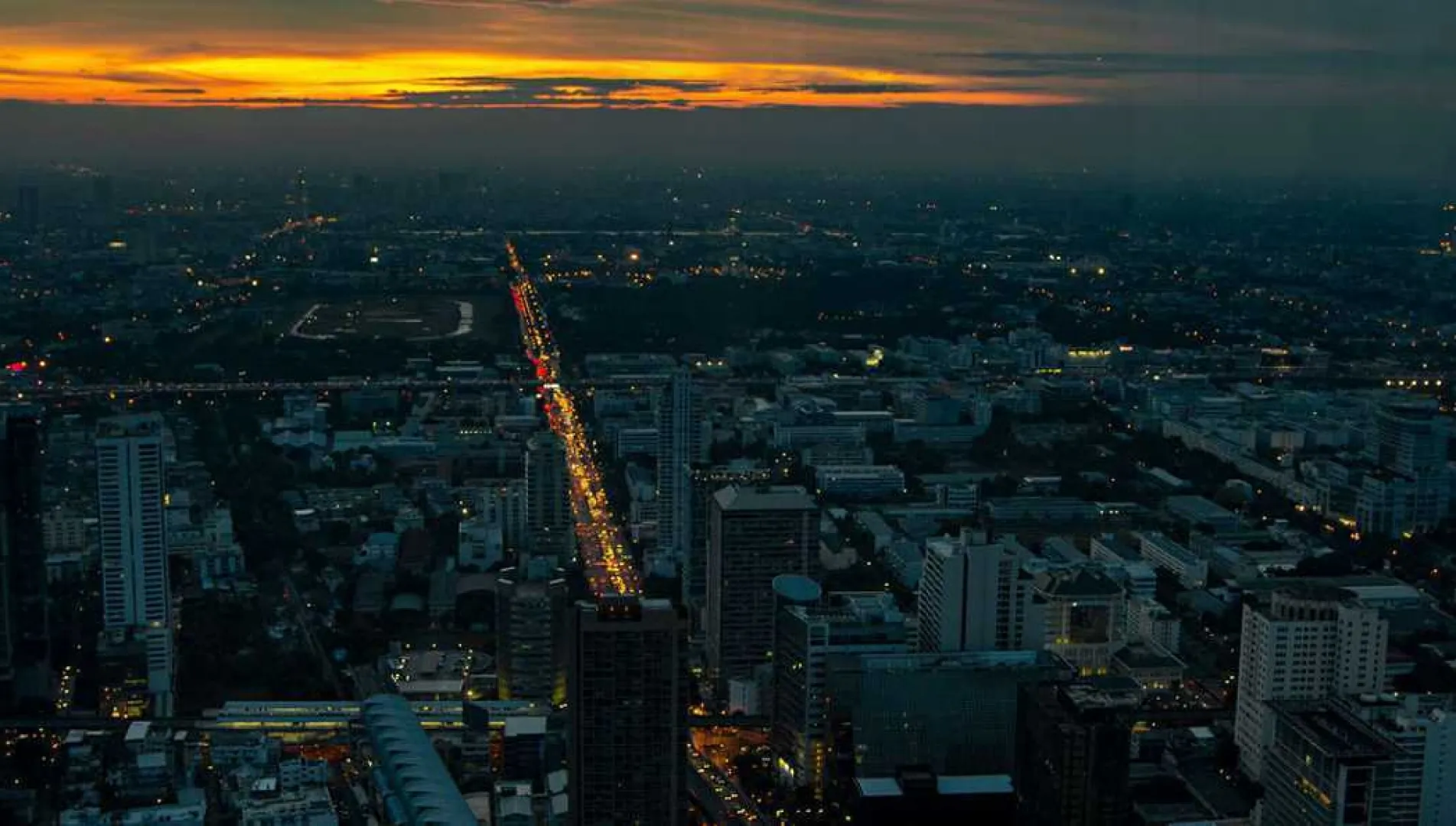 Aerial view of a commercial cityscape at dusk with illuminated buildings and a glowing traffic corridor, symbolizing income generation opportunities through commercial real estate investment in India.
